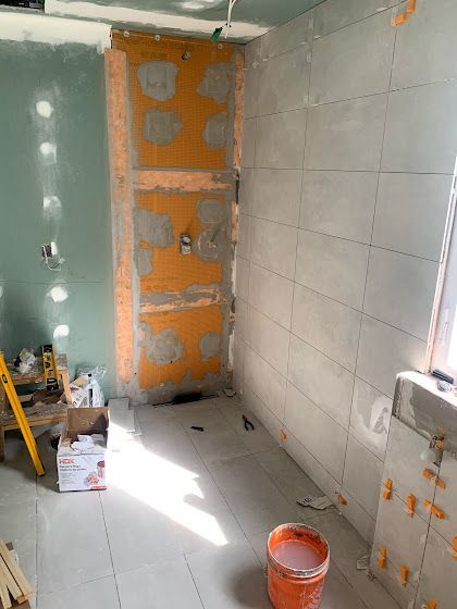Bathroom remodel in progress: tiled wall, orange-colored waterproof membrane, and drywall.