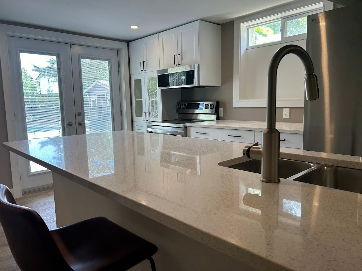 Modern kitchen with white cabinets, stainless steel appliances, and a quartz countertop island.
