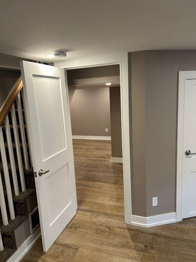 Interior view: open doorways, staircase, wood-look flooring, neutral walls, white doors.