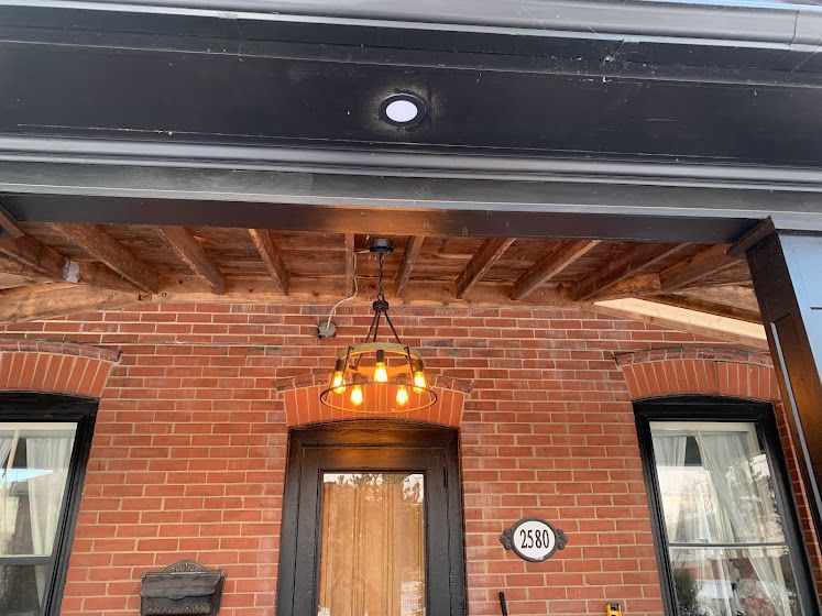 Brick building entrance with wooden ceiling, pendant light, and two windows.