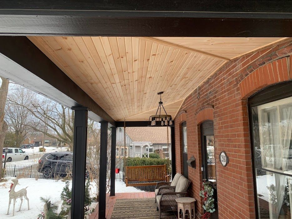 Porch with new wood ceiling, black beams, brick wall, swing, and snow on the ground.