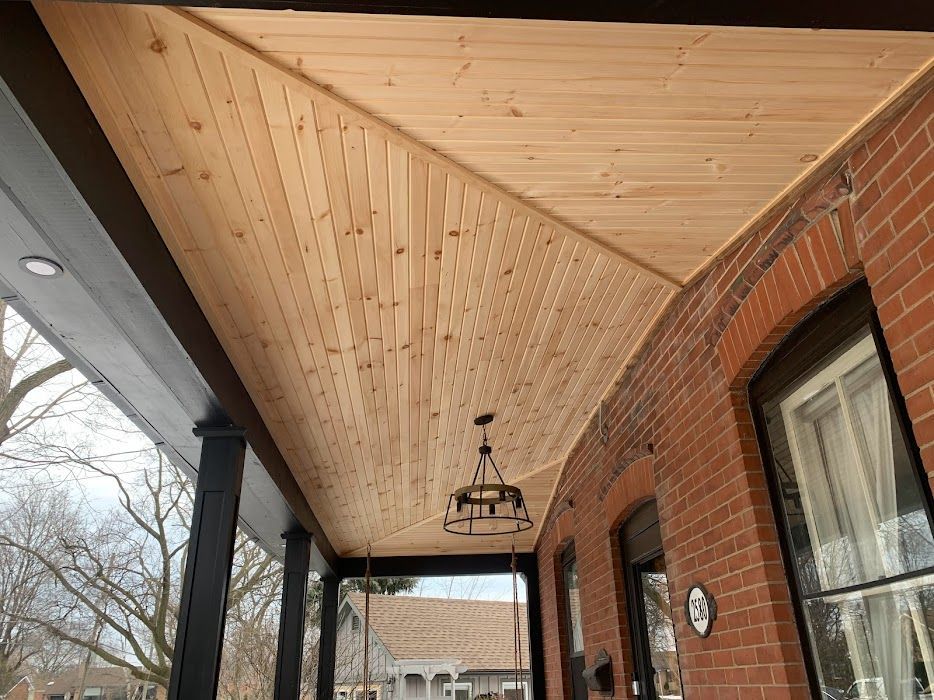 Wood ceiling of a porch with black supports and red brick wall.