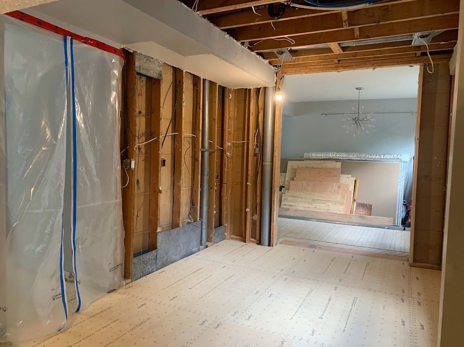 Room under renovation, exposed studs, plastic sheeting, unfinished floor, doorway to another room.