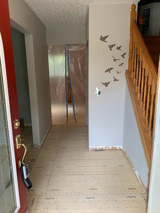 Entryway with new light flooring, gray walls, red door, wooden staircase, and bird wall decal.