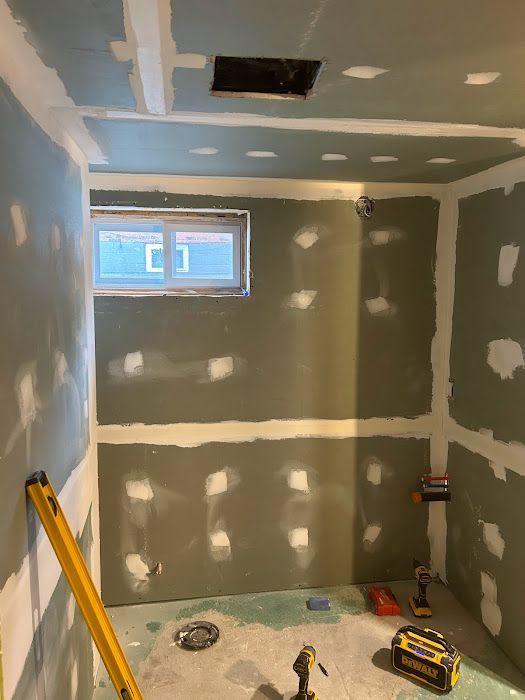 Bathroom renovation in progress; drywall installed, mudded. Window, vent, and plumbing fixtures visible.