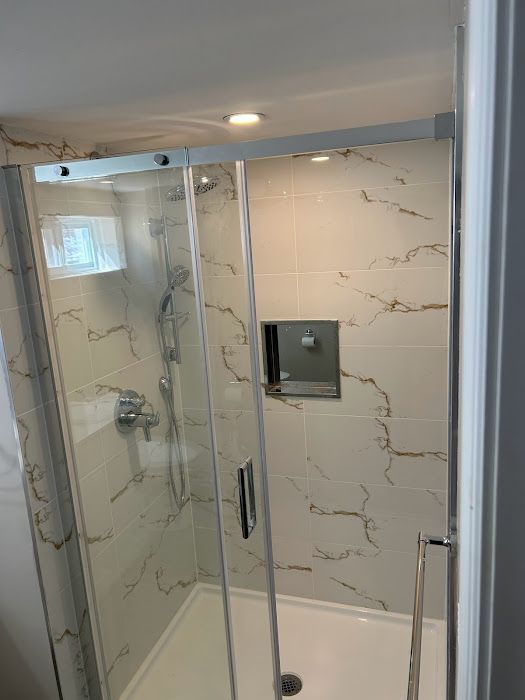 Modern shower with glass doors and marble-look tile walls, recessed shelf, and chrome fixtures.