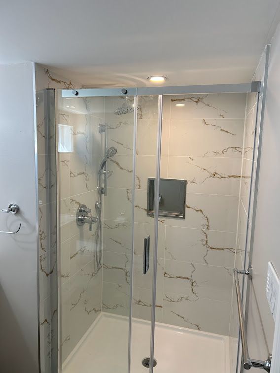 Modern shower with glass doors, marble-look tile, and chrome fixtures.