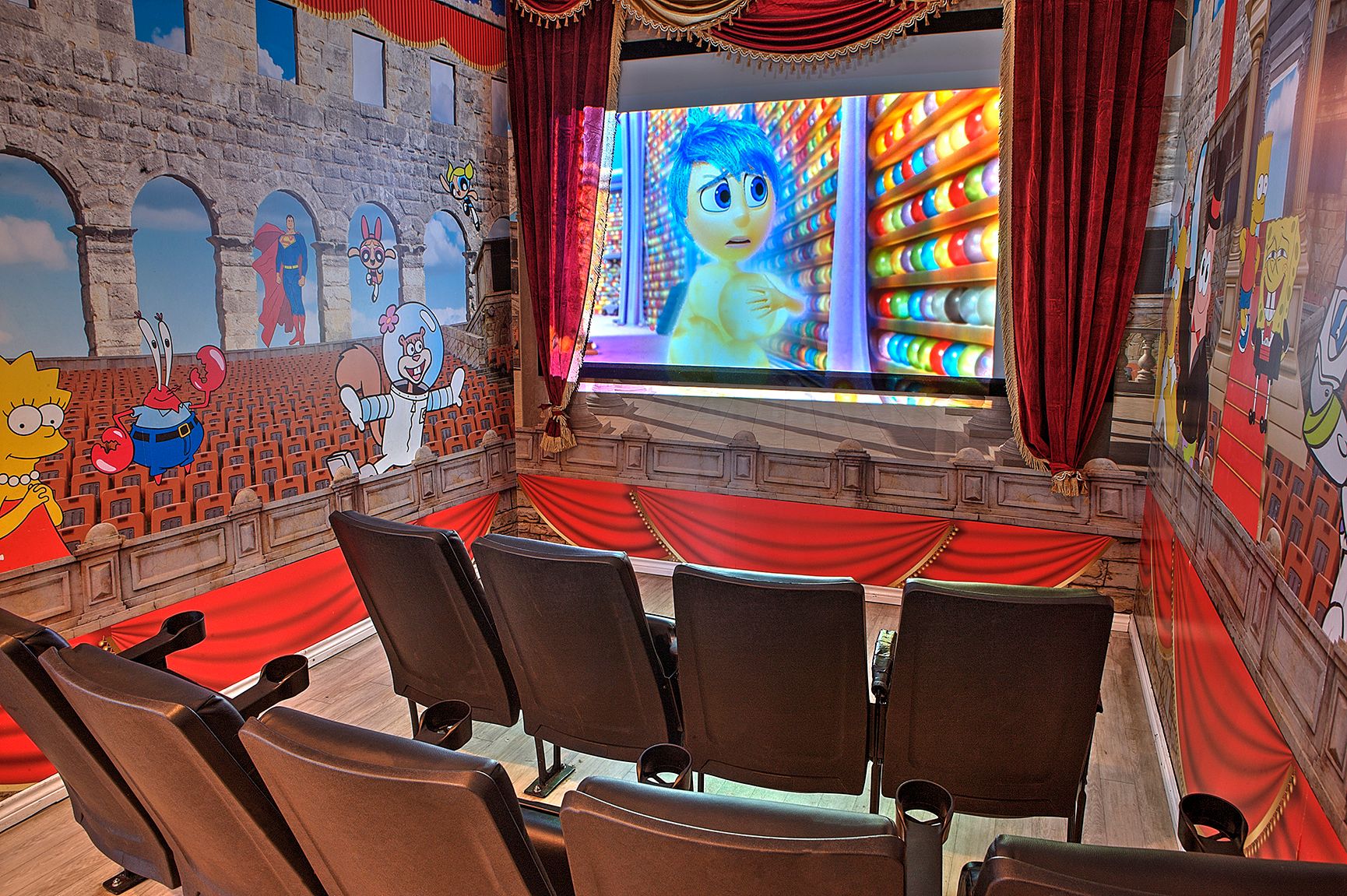 Empty theater with red curtains and seats facing a screen showing a blue animated character.