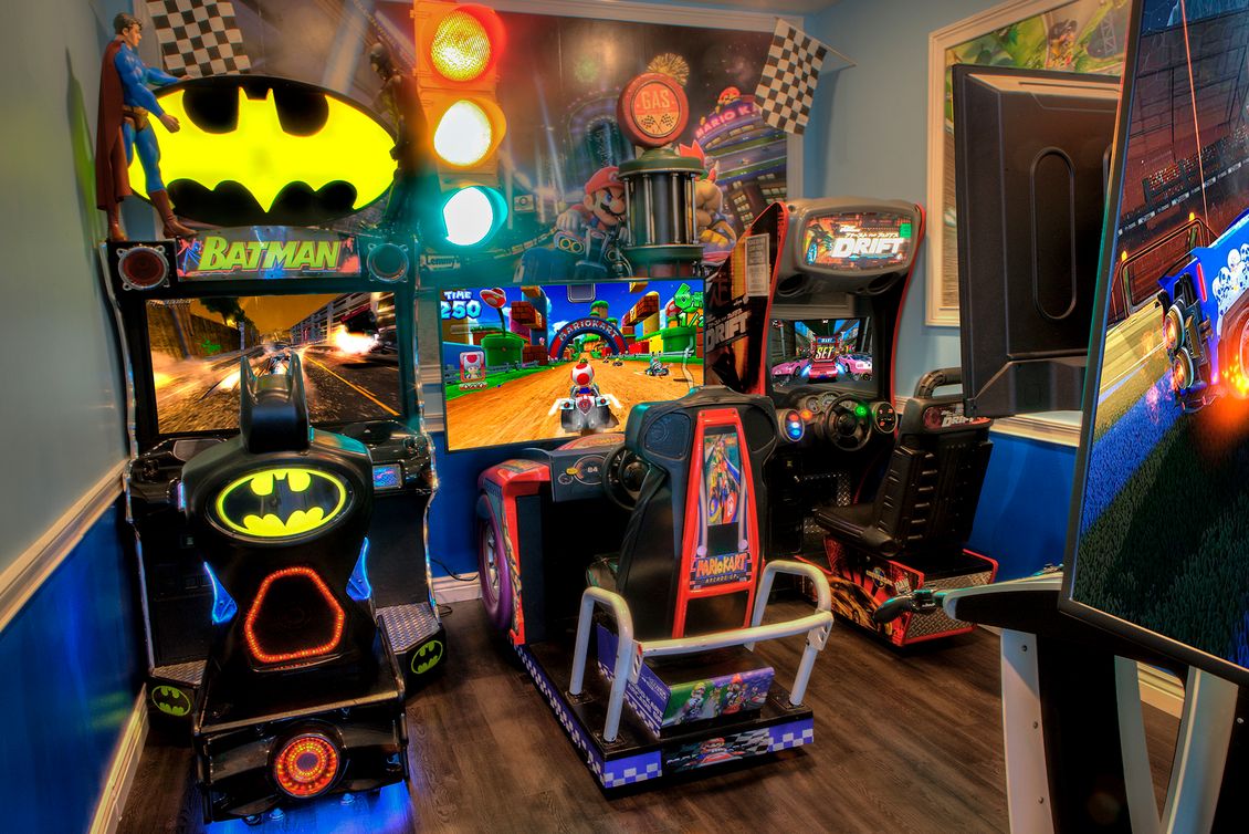 Colorful arcade room with Batman pinball, game cabinets, and a racing game screen
