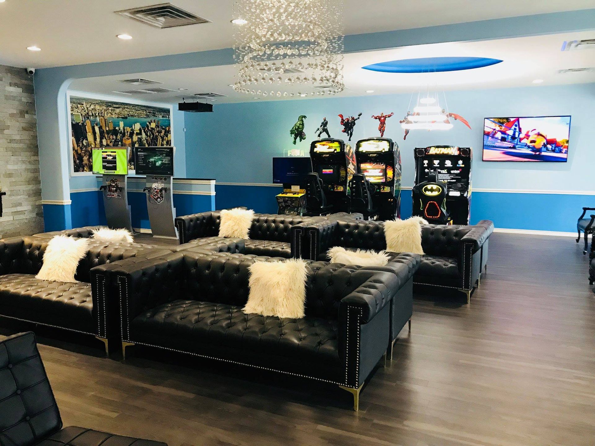 Modern lounge with black sofas, white pillows, arcade machines, and a wall-mounted TV in a blue room