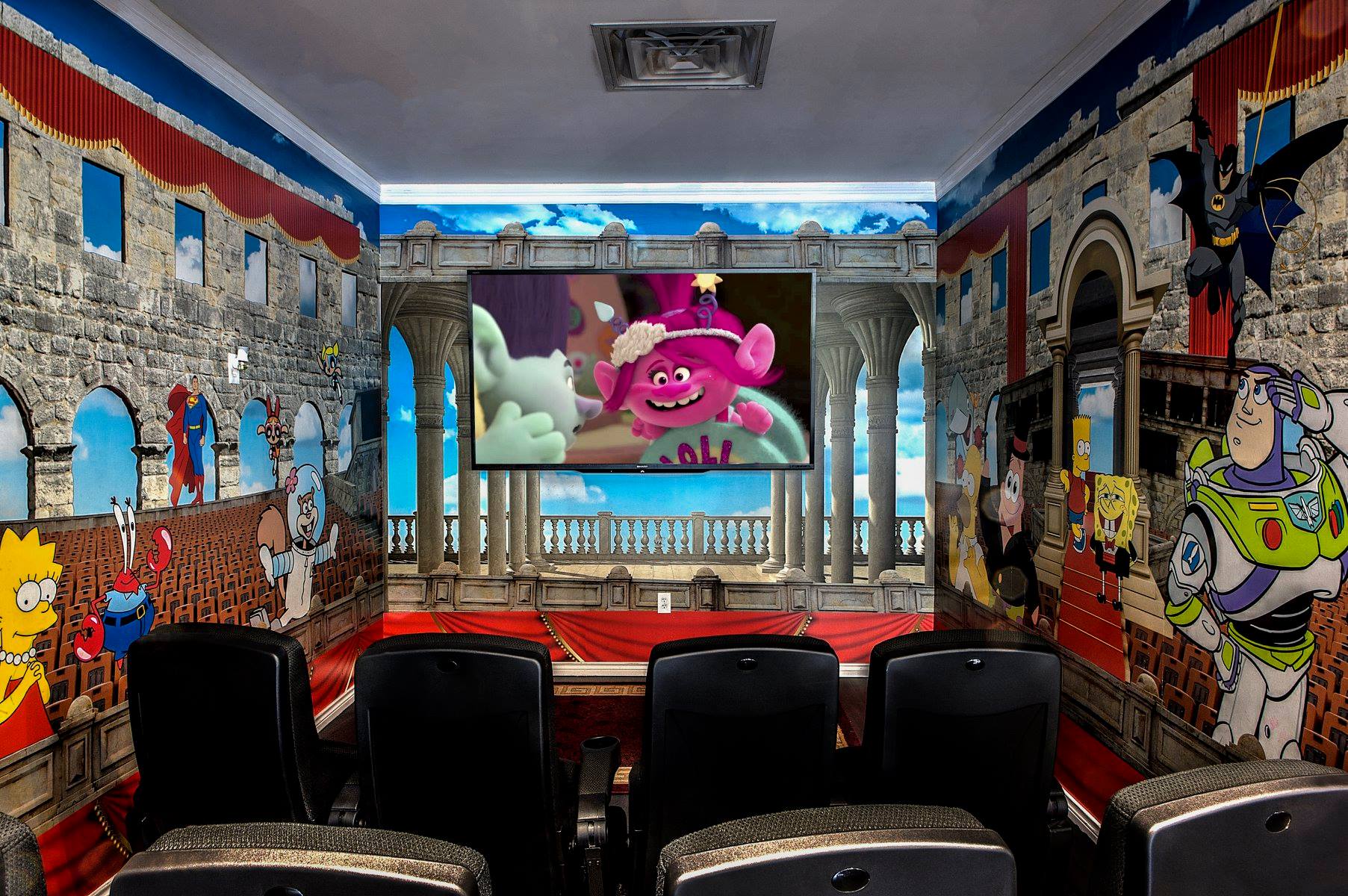 Graffiti-covered screening room with rows of black seats and a large TV showing a pink cartoon character