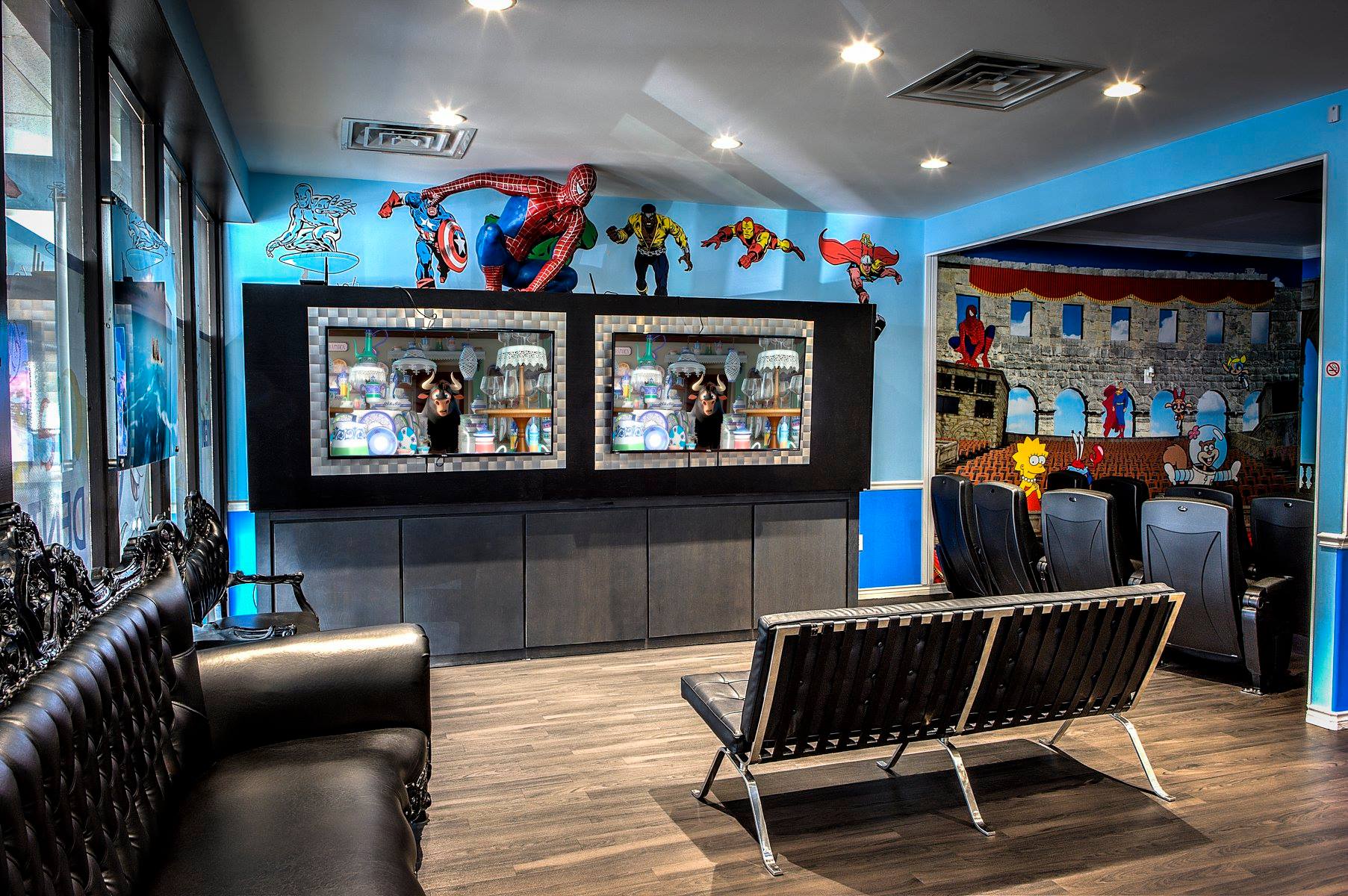 Modern lounge with arcade screens, superhero wall art, black seating, and bright blue accents