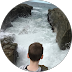 Person looking over a calm river between rocky cliffs, viewed from behind.