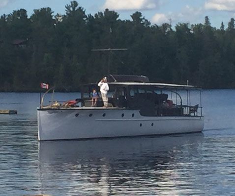 A white motor yacht with a Canadian flag cruises on calm water against a backdrop of a dense pine forest.