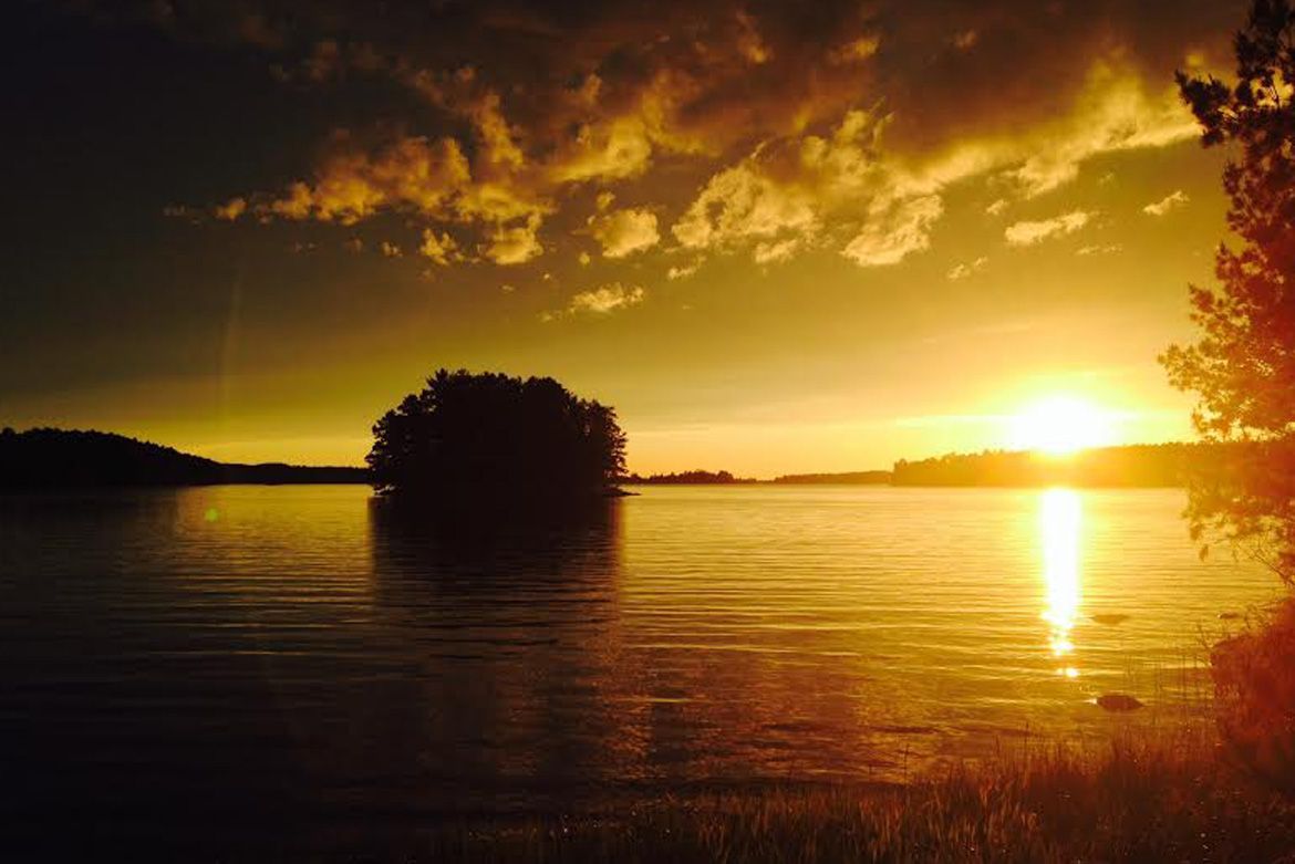 Golden sunset over a calm lake with a silhouetted island in the center and trees on the far shore.