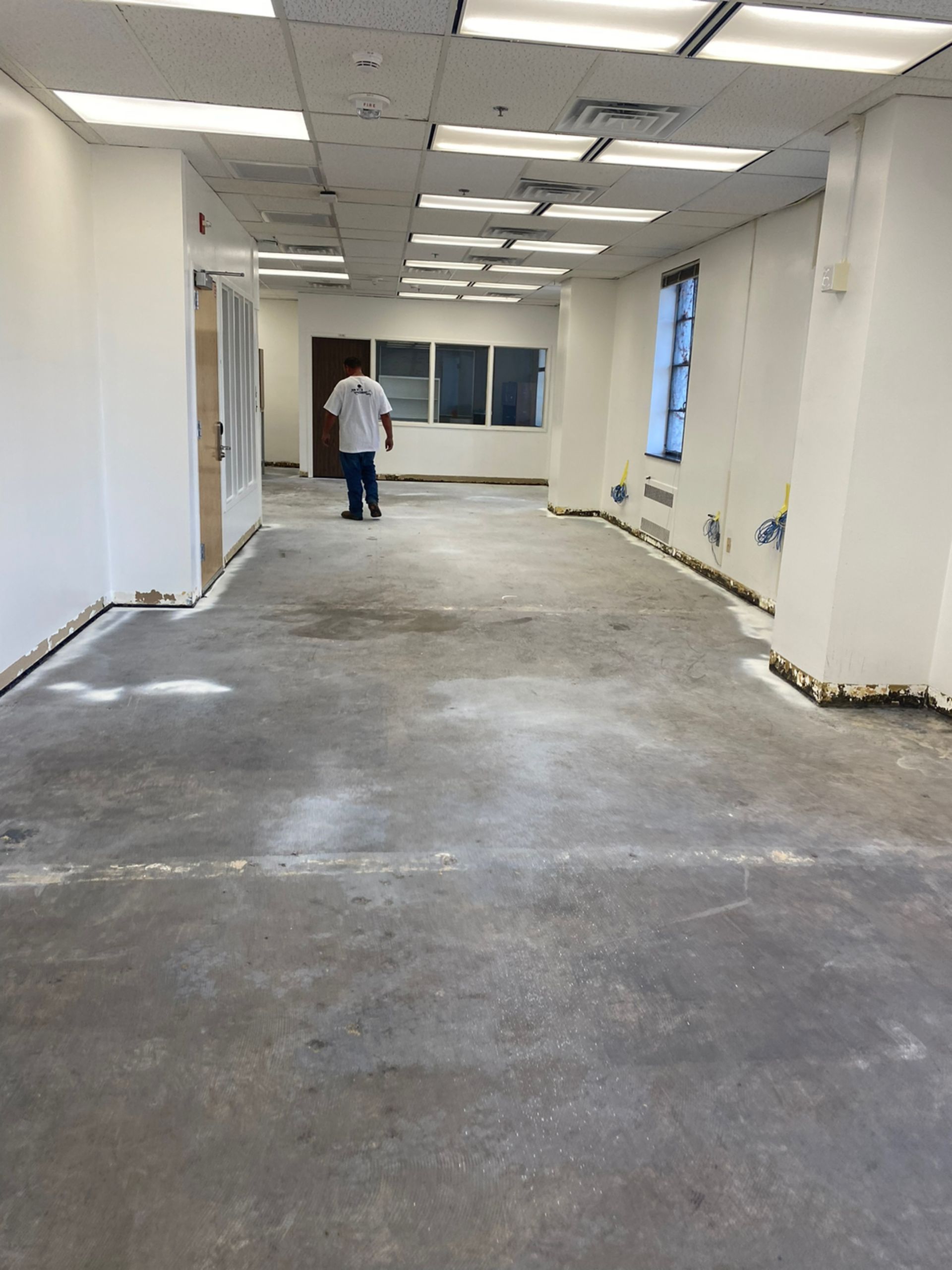 An empty, open office space with exposed concrete floor, a person standing in the distance.