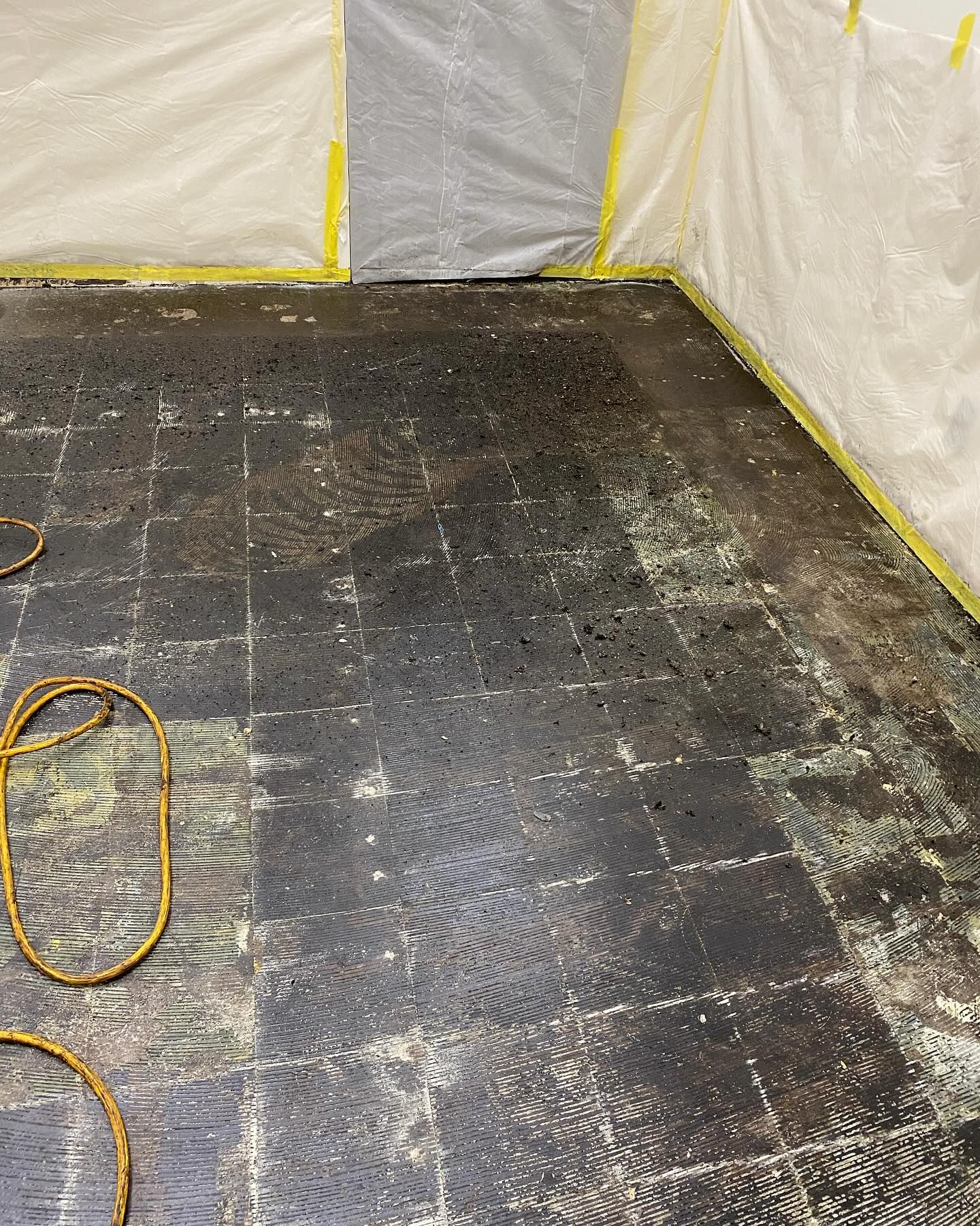 Black and white tiled floor covered in debris, protected by plastic sheeting in a confined space.