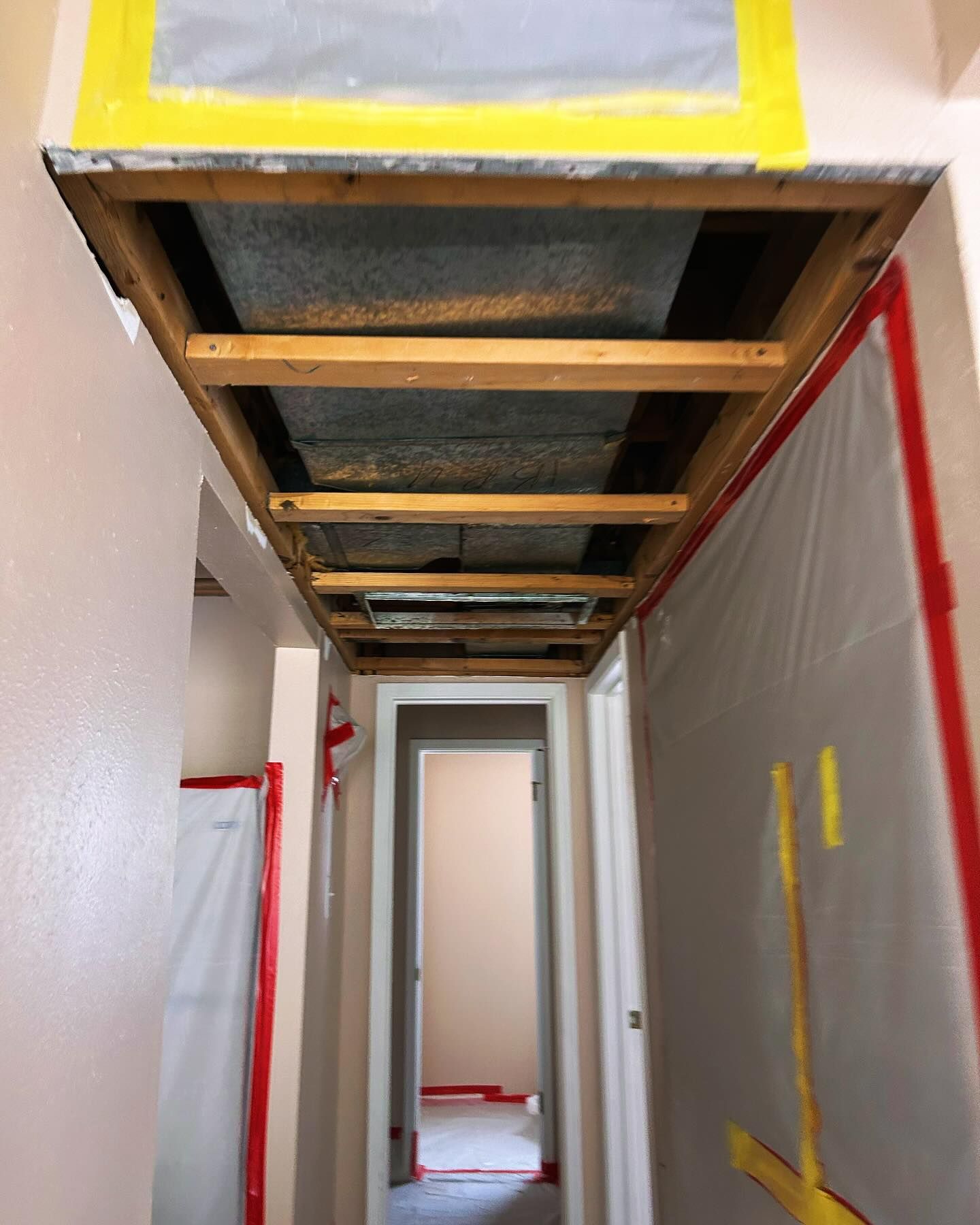 Hallway ceiling repair: exposed wooden beams, plastic sheeting, and yellow tape.