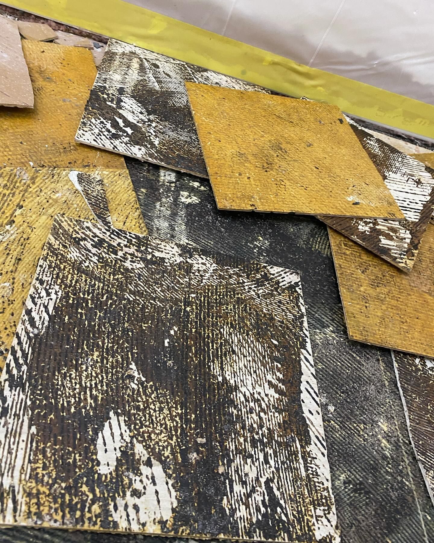 Overhead view of removed brown and black tiles on a floor, revealing the underlayment.