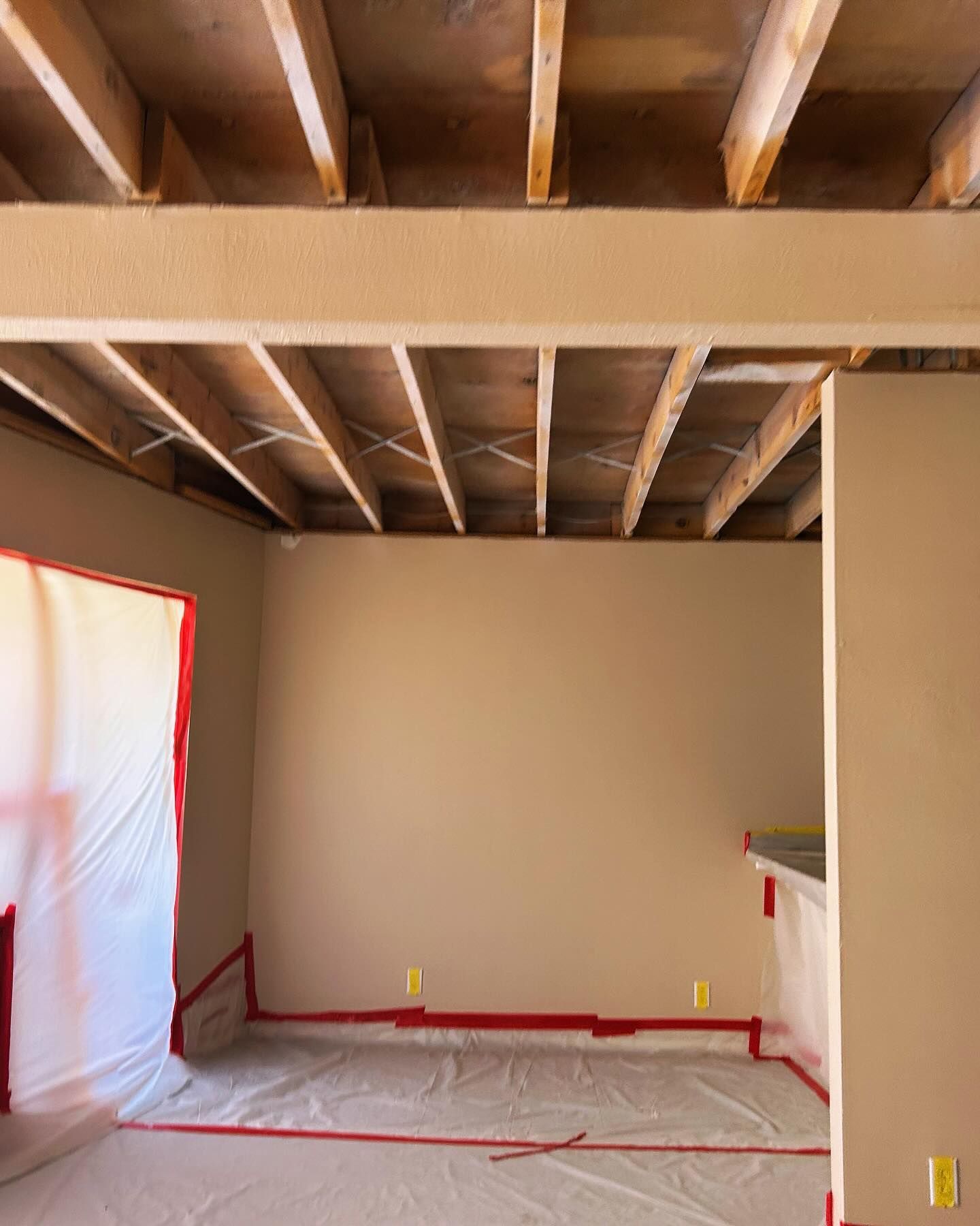Room under construction with exposed wooden beams, walls, and plastic sheeting.