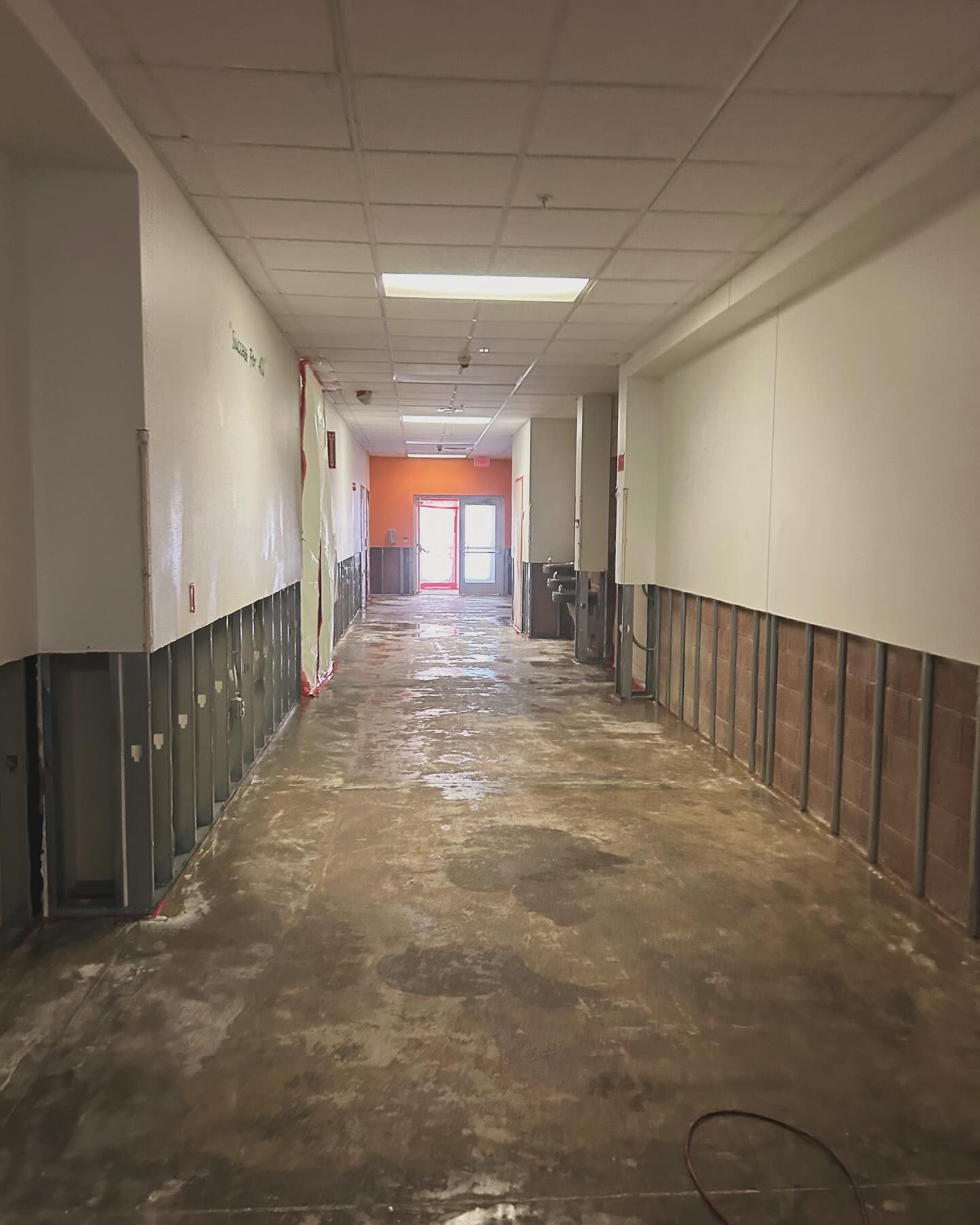 Renovated hallway with exposed wall studs, concrete floor, and orange doorway.