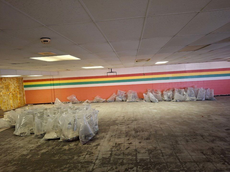 Room with clear plastic bags, possibly debris, lined along the walls. Red, yellow, and green stripes painted on the walls.