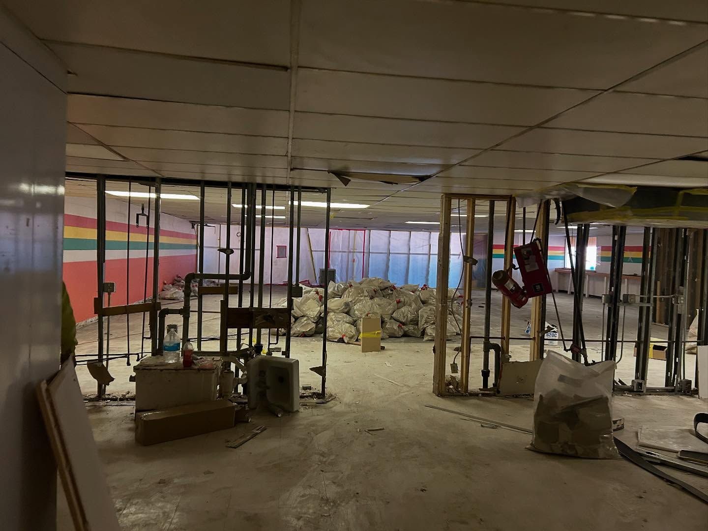 Interior demolition site with exposed wall frames, debris, and damaged ceiling.
