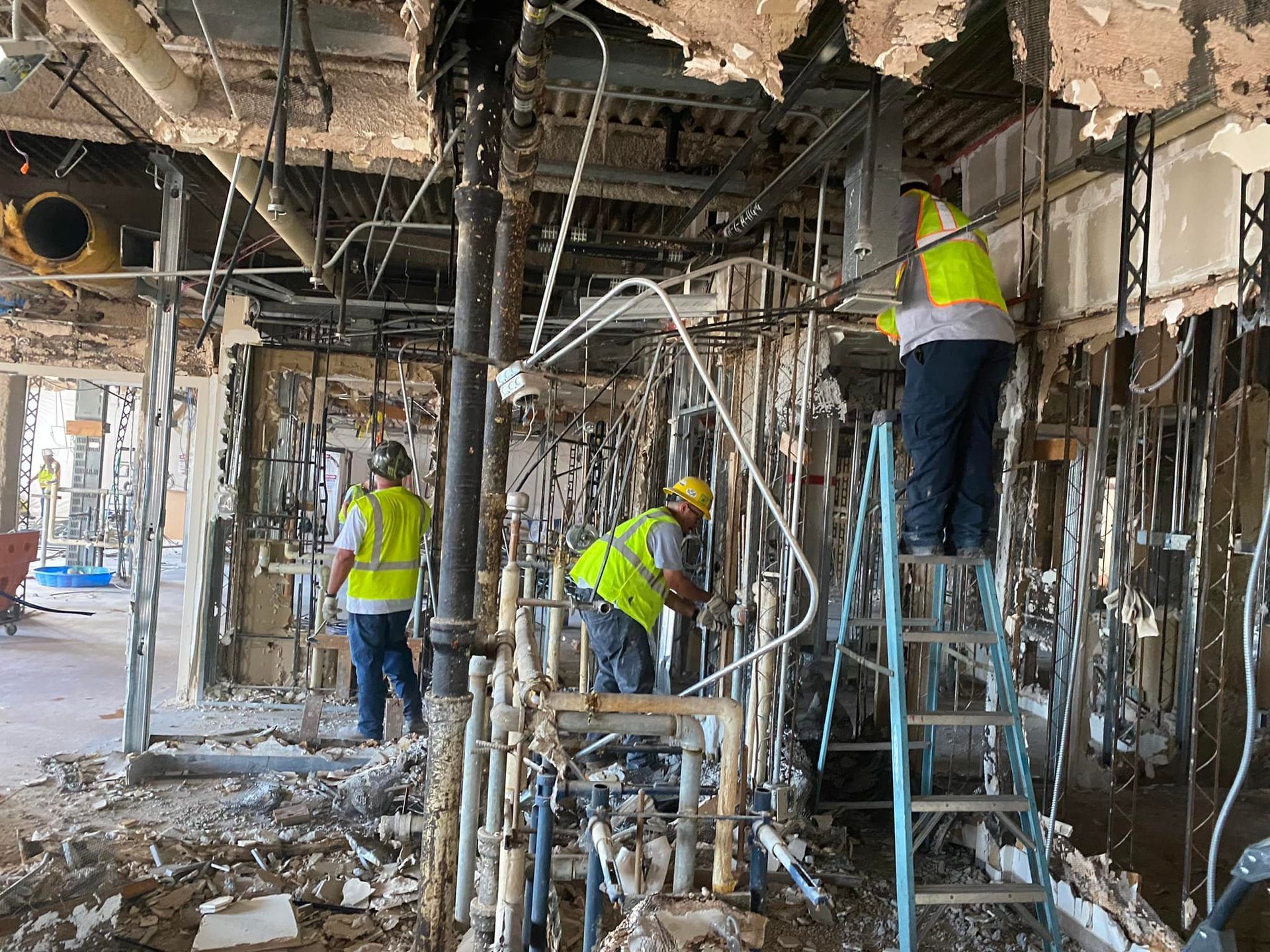 Construction workers in a building, wearing safety vests, removing pipes.