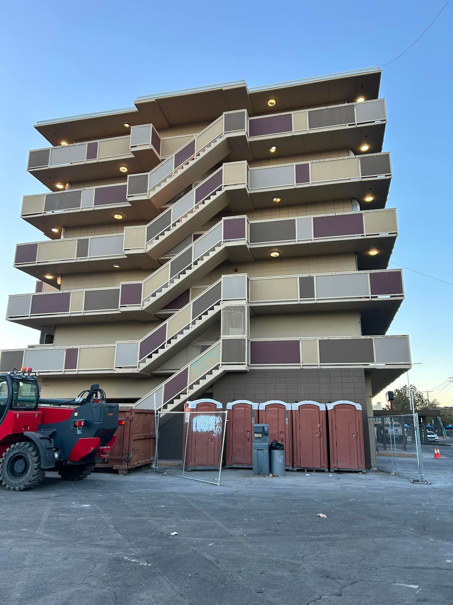 A multi-story building with exterior staircases; a construction site with port-a-potties and a front-end loader.