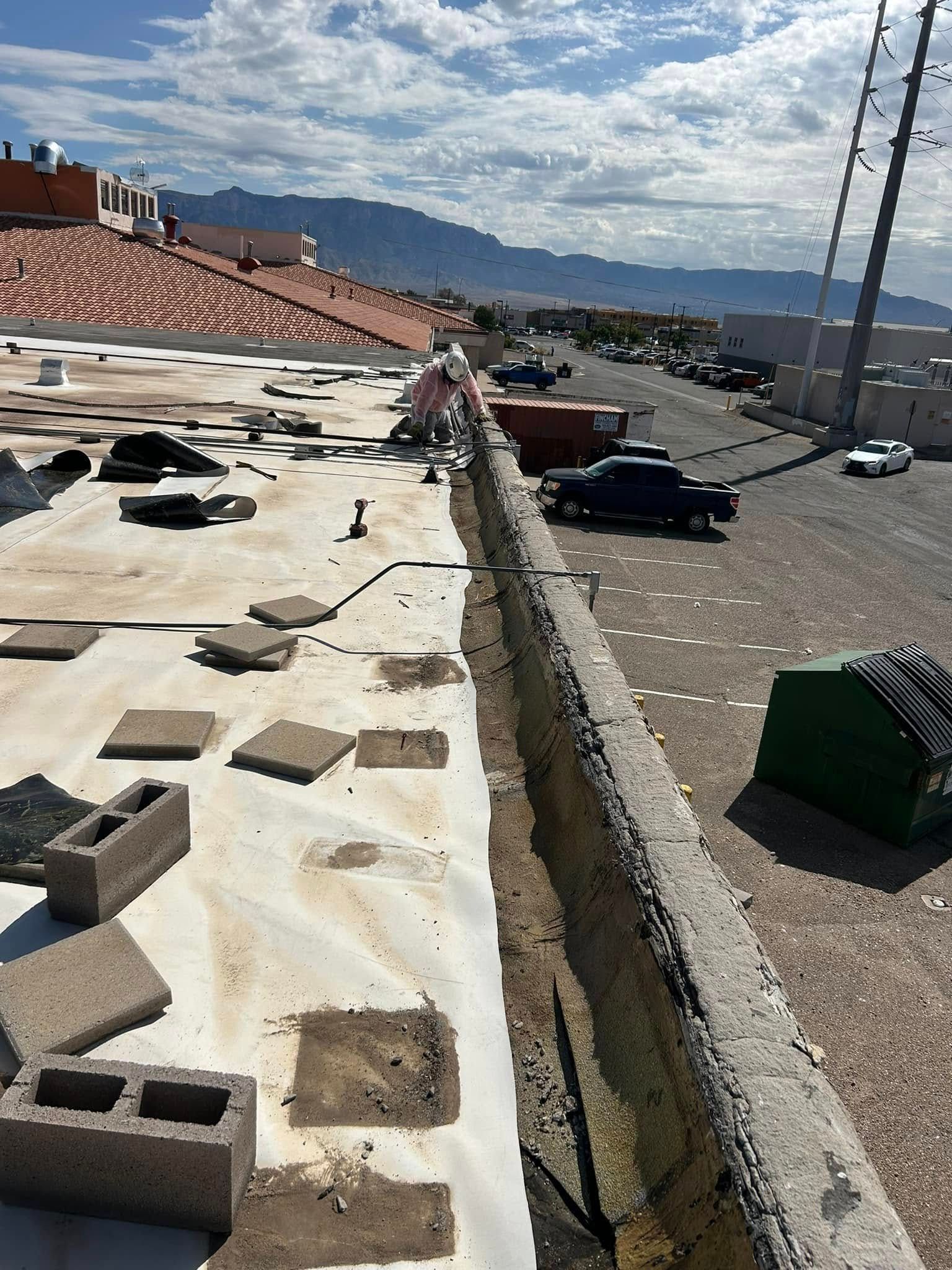 Roof of a building under construction with exposed layers, concrete blocks, and vehicles in background.