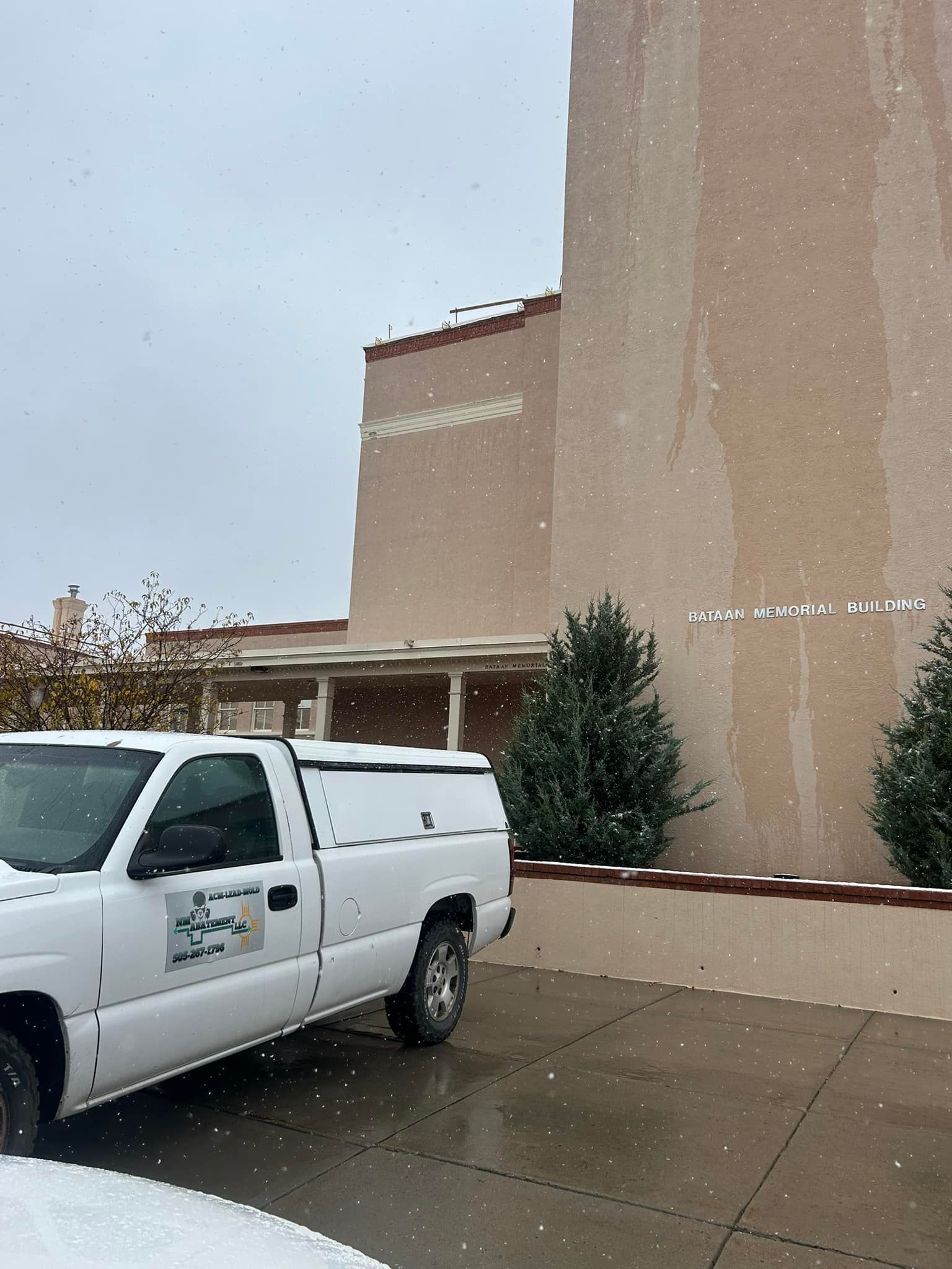 White truck parked in front of a beige building with snow falling.