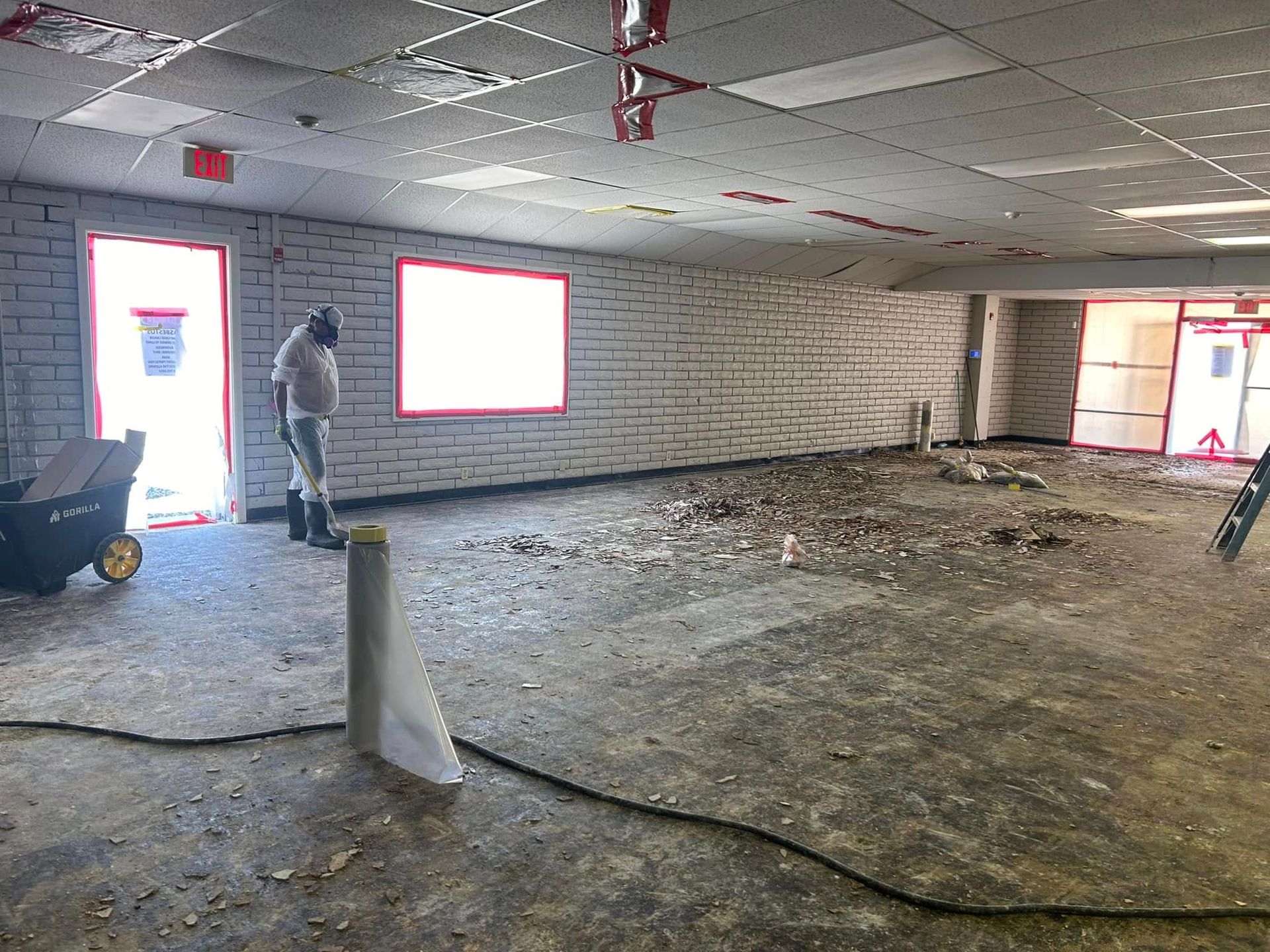 Interior of a construction site. A worker stands near a window and debris covers the floor.