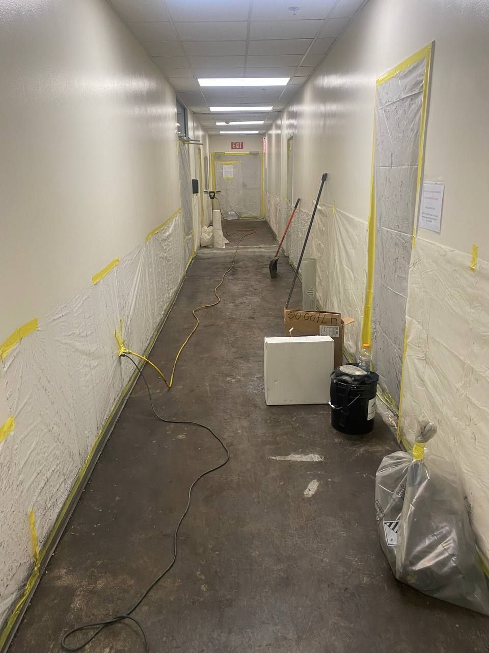 Hallway under construction: plastic sheeting on walls, tools, debris on floor.