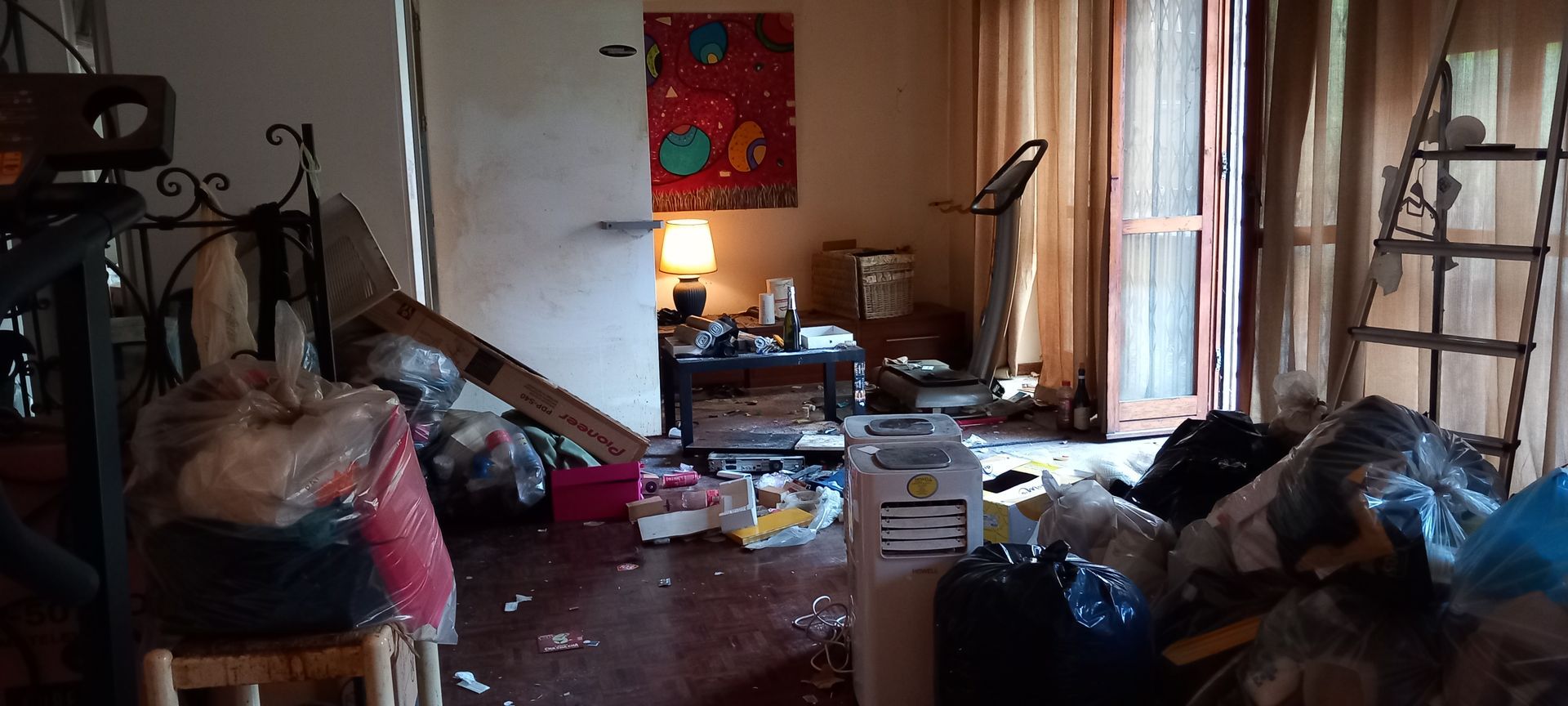 Garage disordinato con armadietti portautensili rossi, vestiti appesi, scaffali e scatole di cartone.