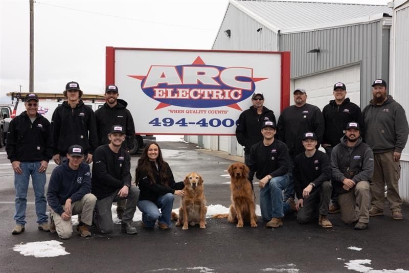 ARC Electric team with two dogs, posing in front of their sign.