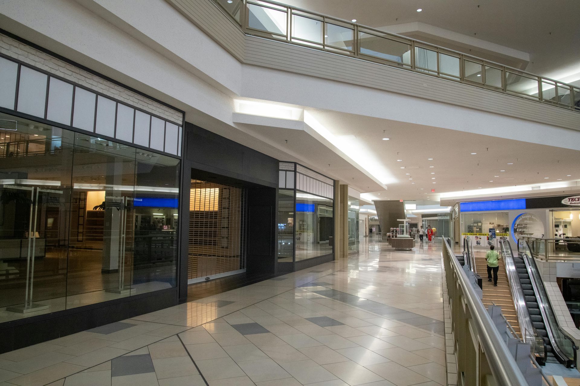 Empty shopping mall corridor with glass storefronts and escalators on the right