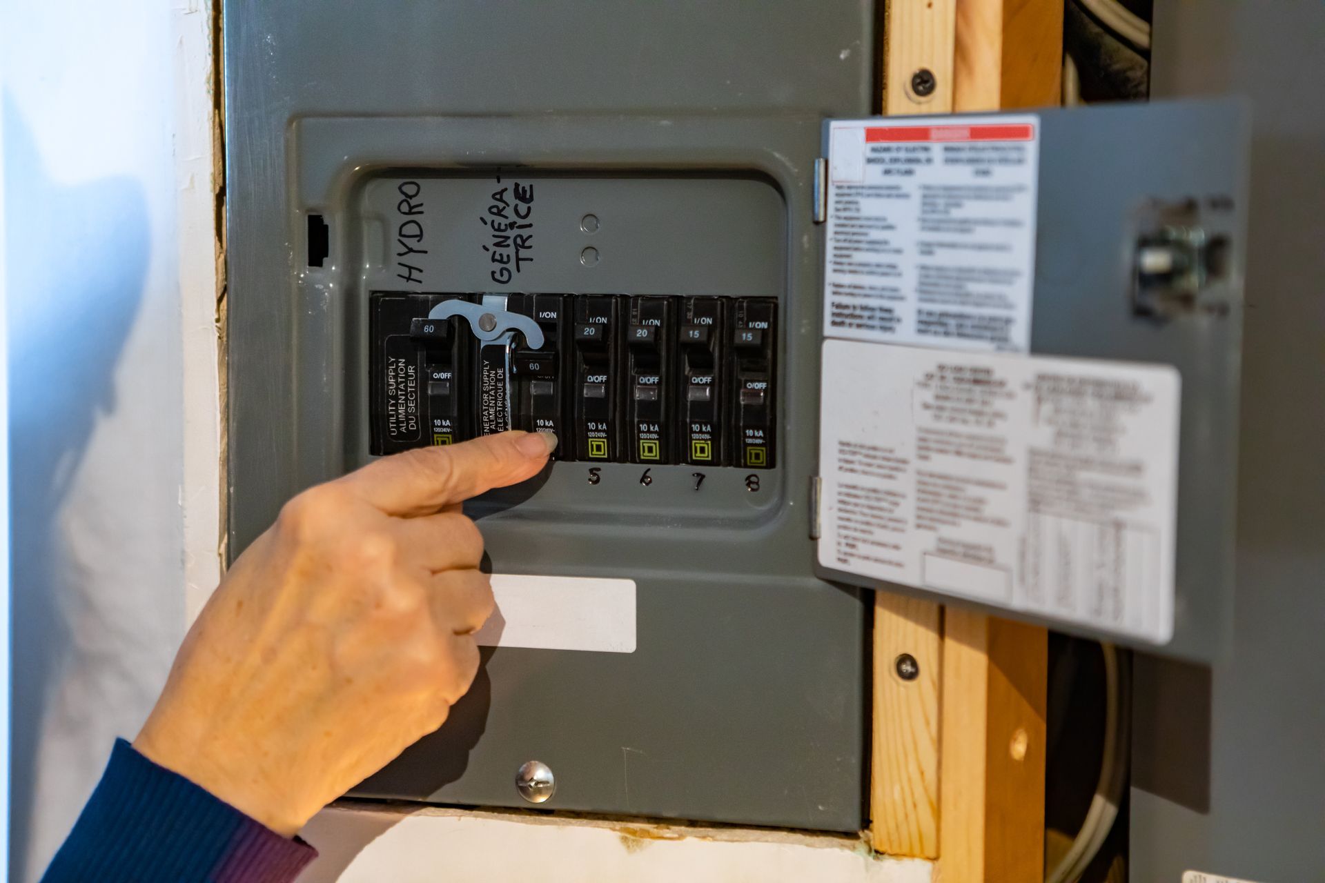Person's finger points at a circuit breaker in a gray electrical panel, possibly resetting it.