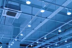 Blue-toned shot of a commercial ceiling with track lighting, air vents, and metal beams.