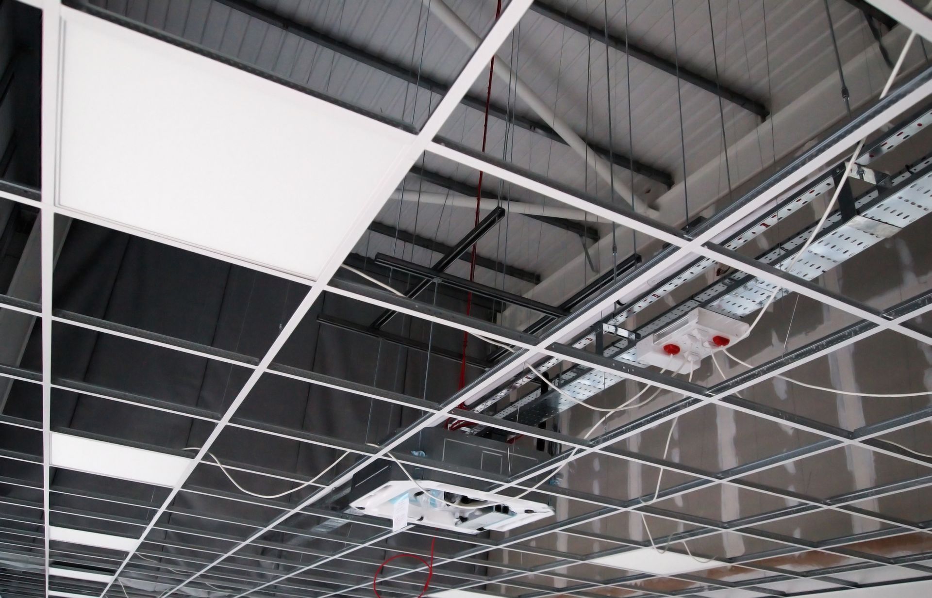 Ceiling of a commercial space with a grid of panels, exposed ducts, and mounted lighting fixtures