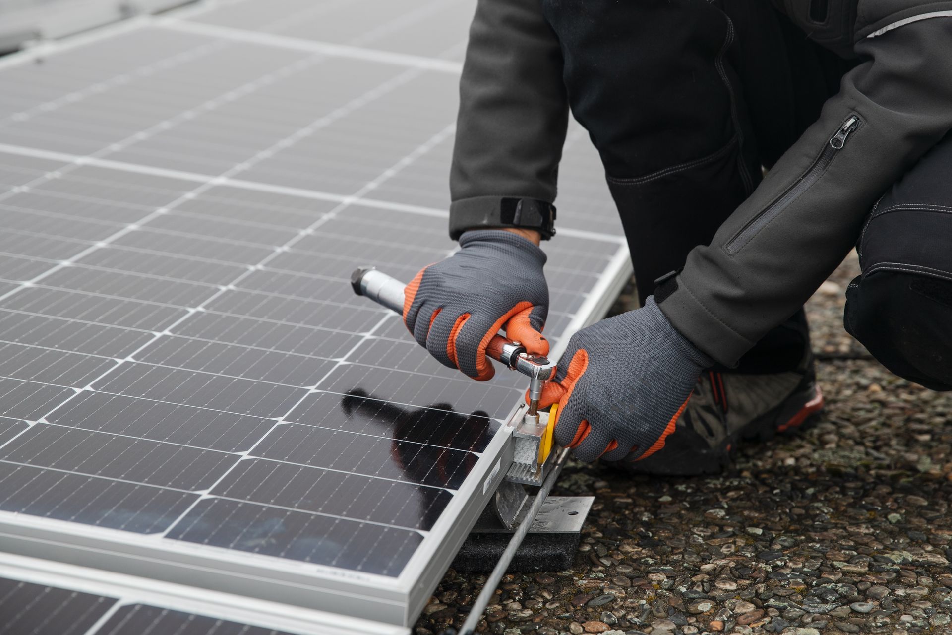 Worker installing solar panels with orange-handled tools on a rooftop