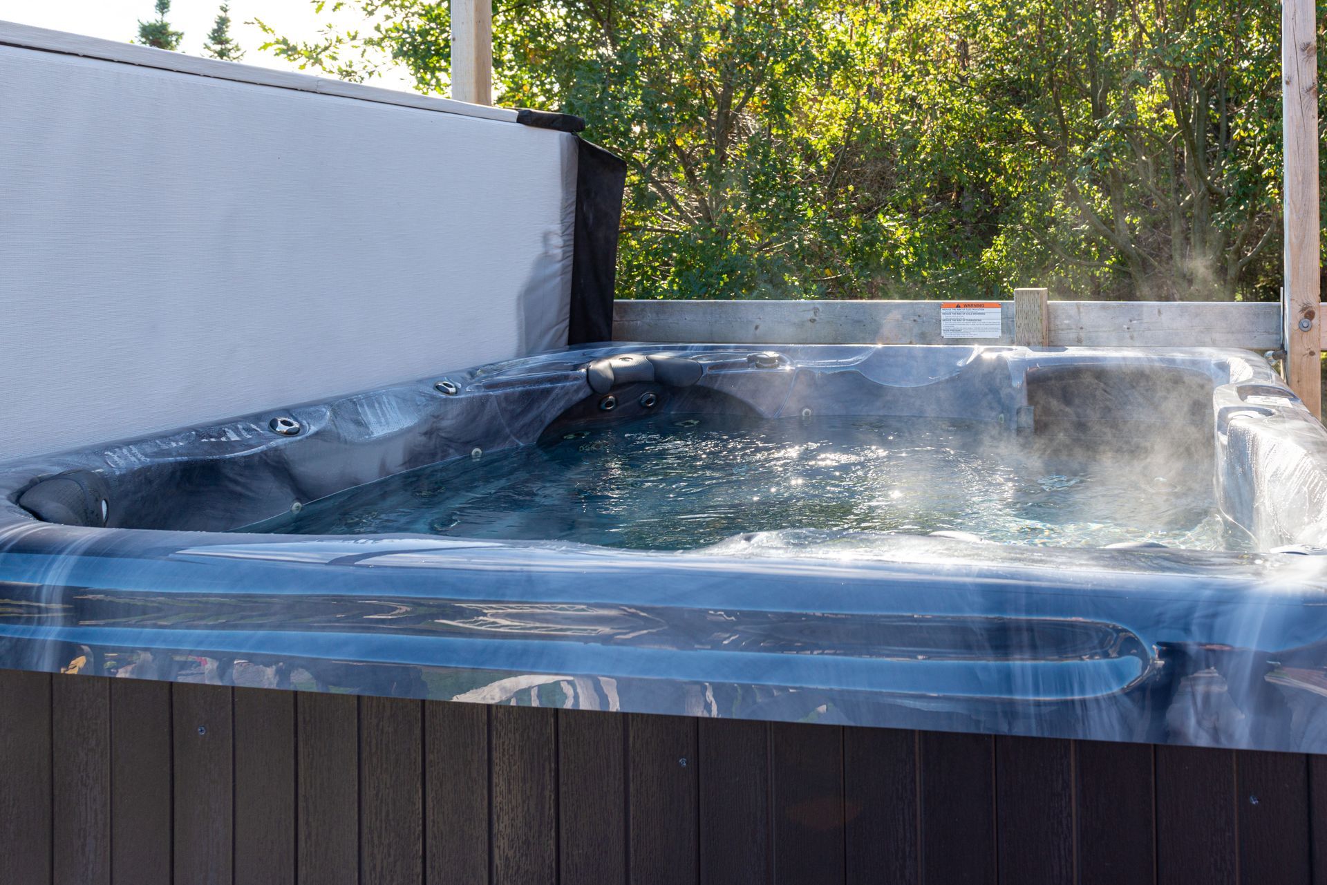 Backyard hot tub with steam rising and water bubbling beside a fence and trees
