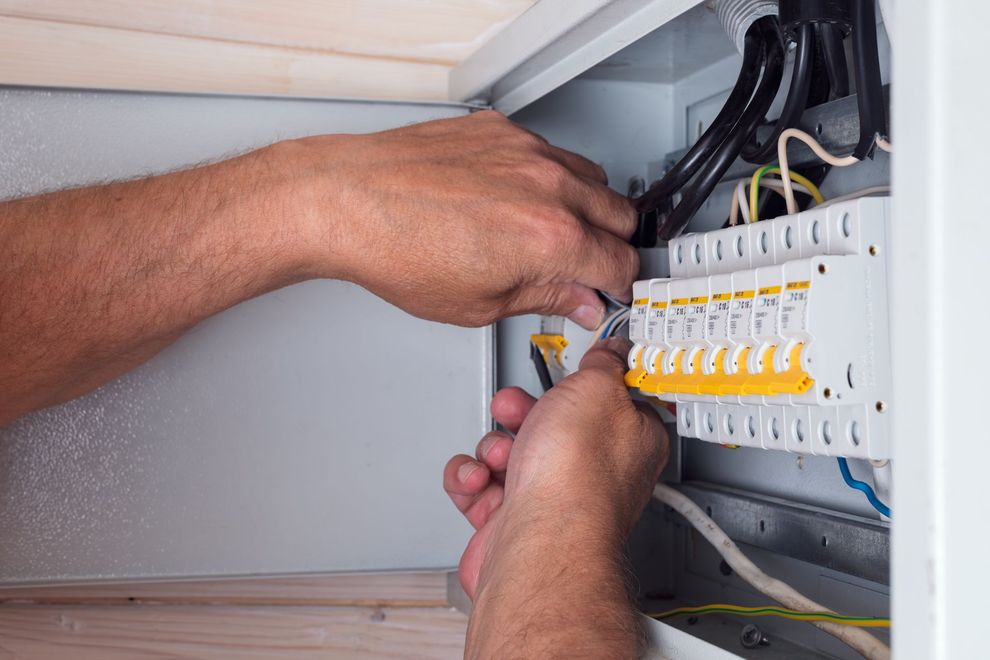 Hands wiring an electrical breaker panel inside a cabinet.