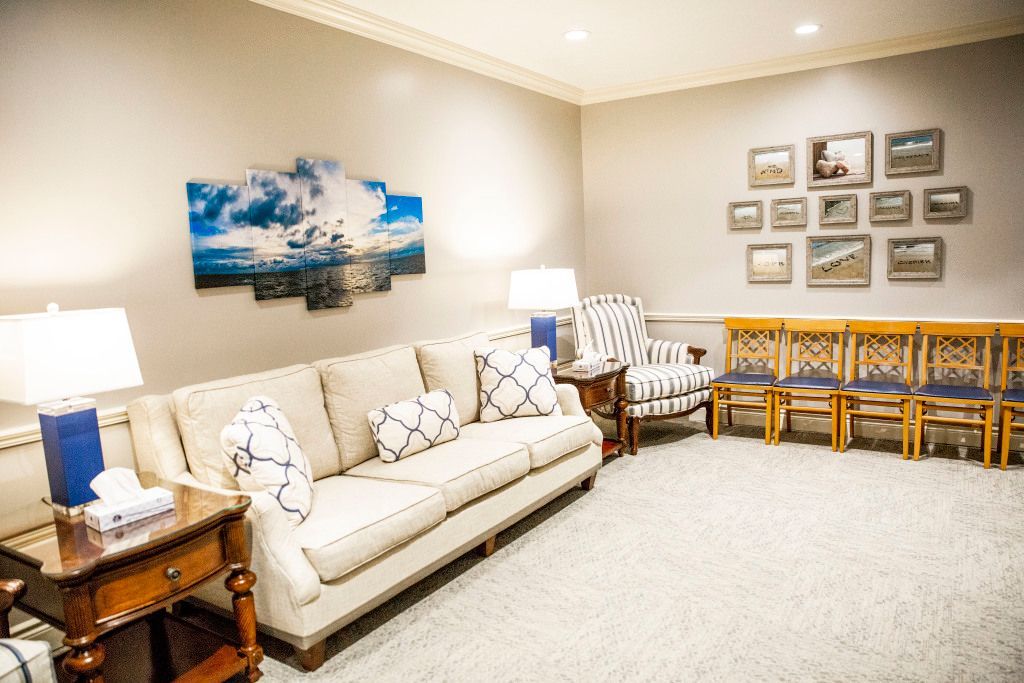 A living room with a couch , chairs , lamps and a painting on the wall.