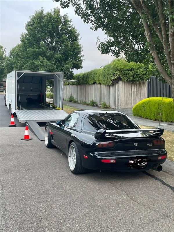 Black sports car near an open trailer on a tree-lined street, with orange cones behind it - Full Throttle Enclosed Car Transport in Kilmore, VIC