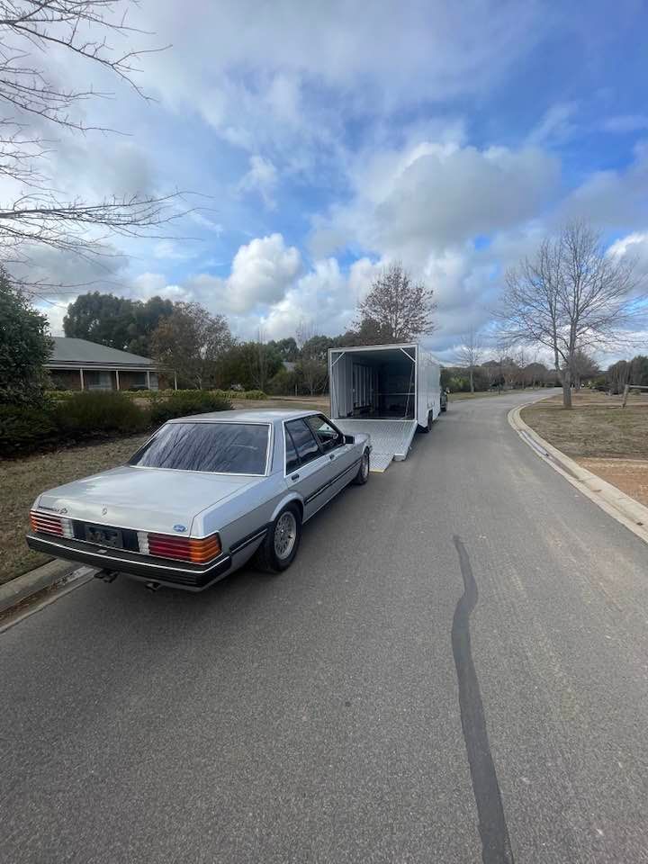 Silver car towing a white enclosed trailer on a paved road under a cloudy sky — Full Throttle Enclosed Car Transport in Kilmore, VIC