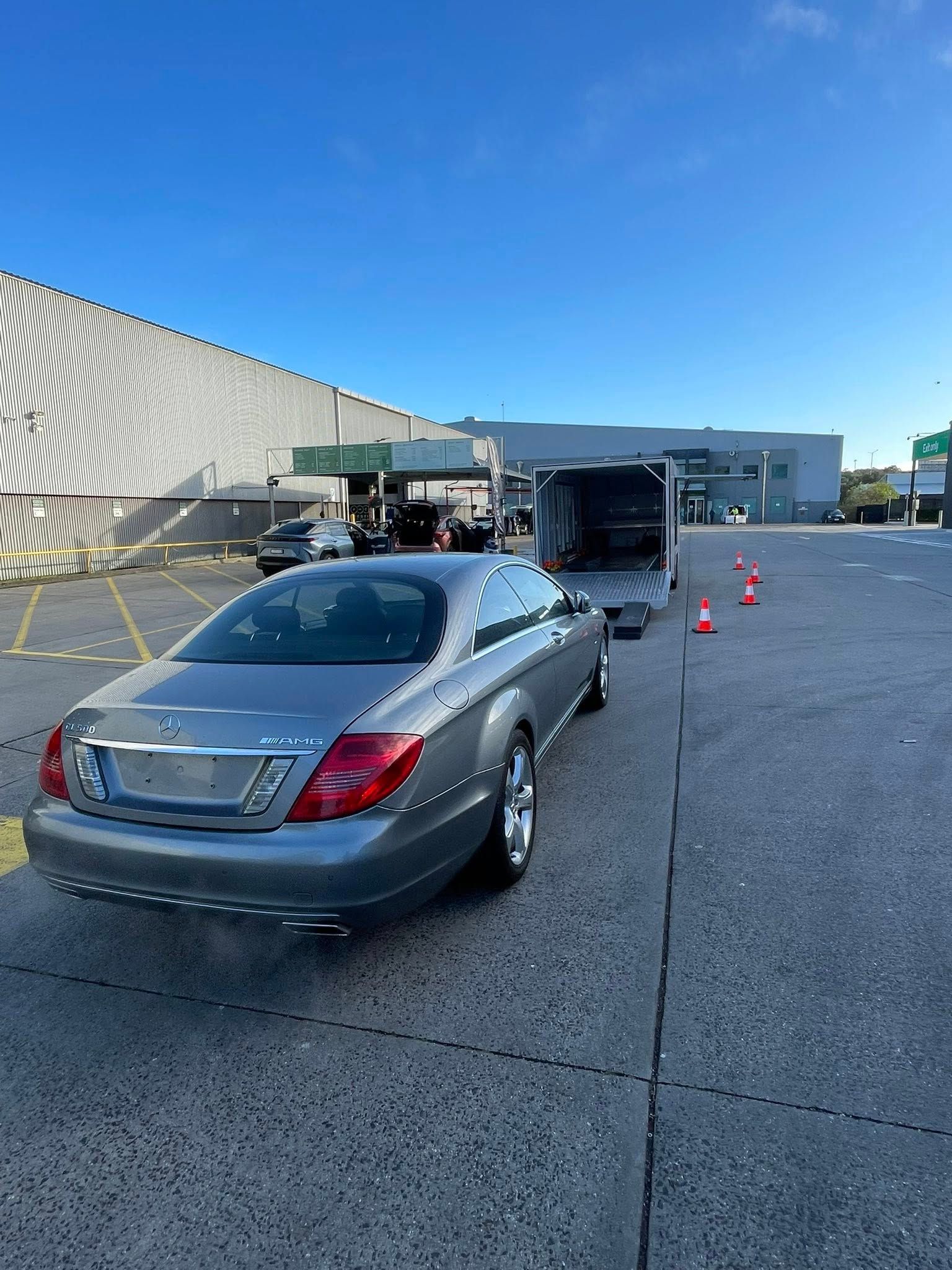 Grey Mercedes-Benz coupe near a trailer on an asphalt lot, under a clear blue sky, next to a large industrial building — Full Throttle Enclosed Car Transport in Kilmore, VIC