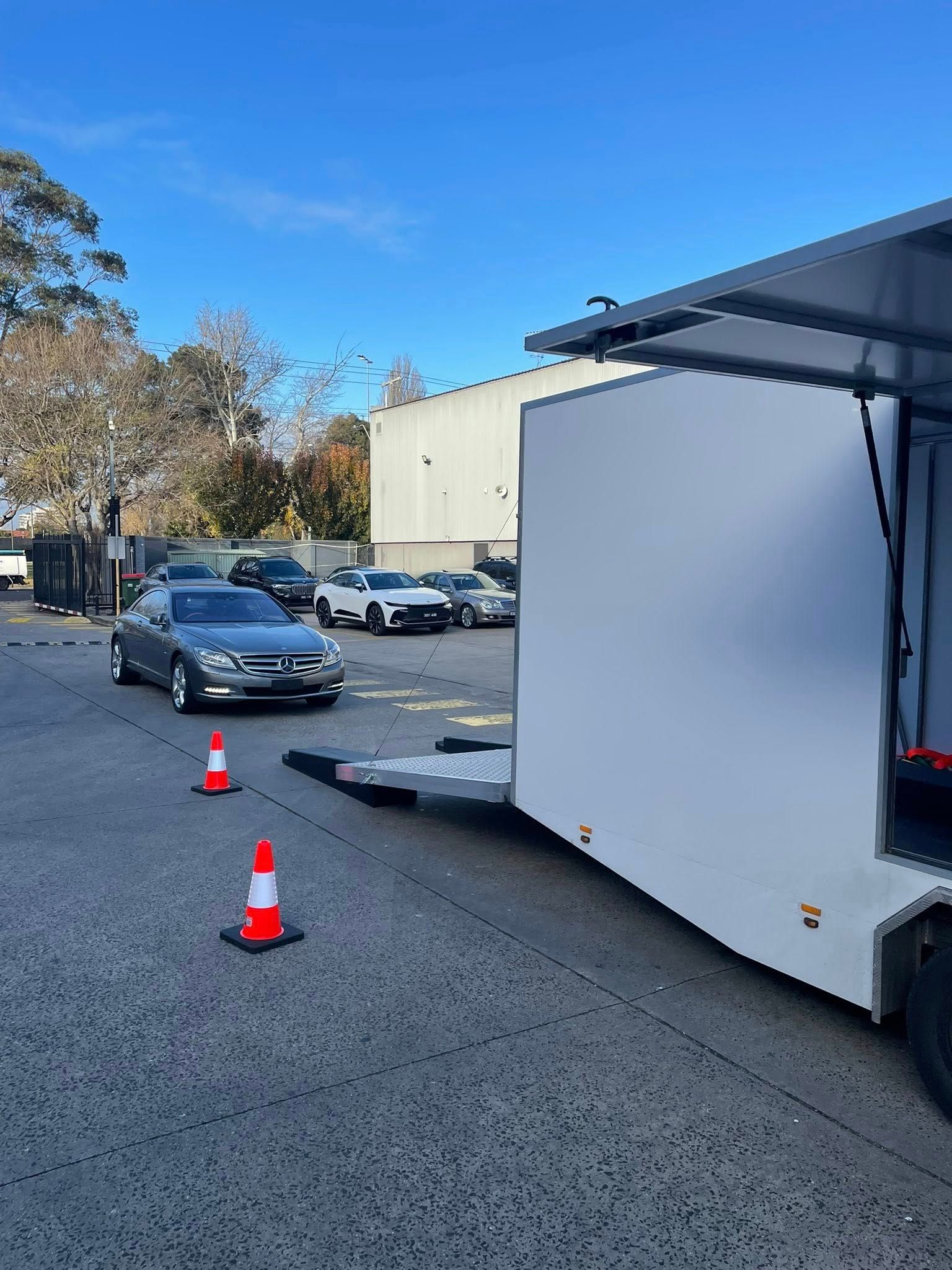Car loading into a white trailer, with other cars parked in the lot on a sunny day — Full Throttle Enclosed Car Transport in Kilmore, VIC