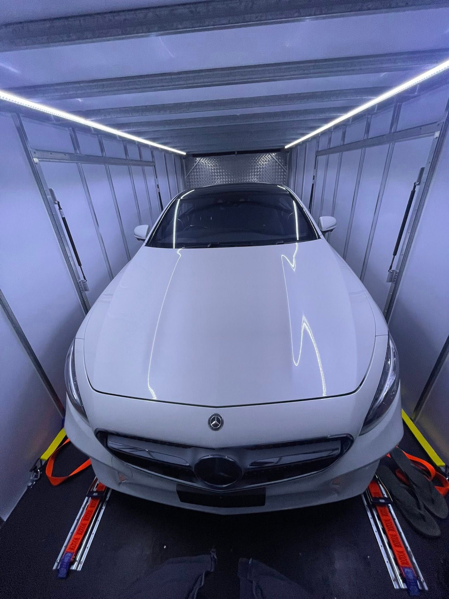 White Mercedes-Benz sedan inside an enclosed car trailer, secured with straps, under overhead lights — Full Throttle Enclosed Car Transport in Kilmore, VIC