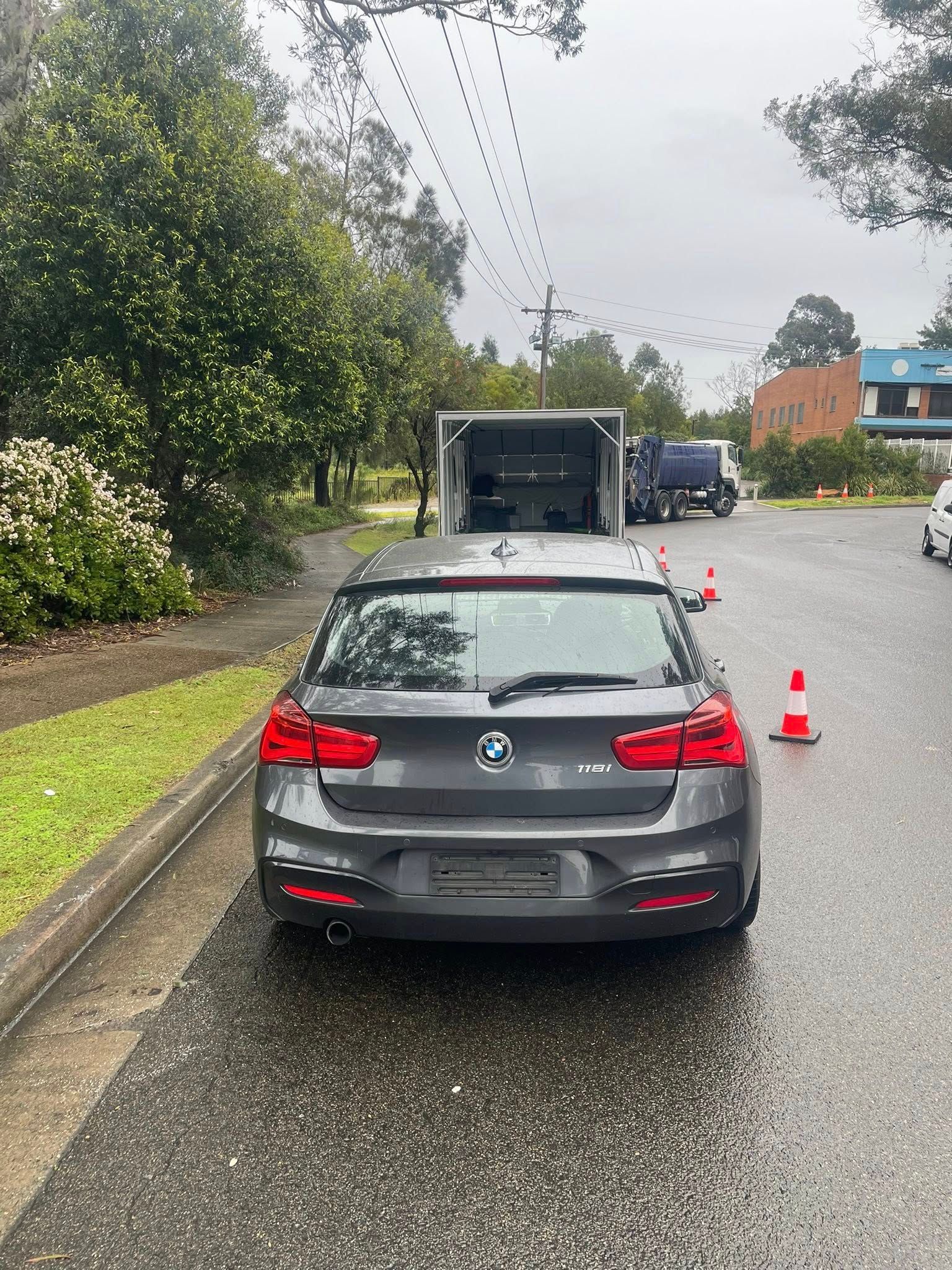 Grey BMW hatchback parked on a wet street with a trailer behind it and a traffic cone — Full Throttle Enclosed Car Transport in Kilmore, VIC