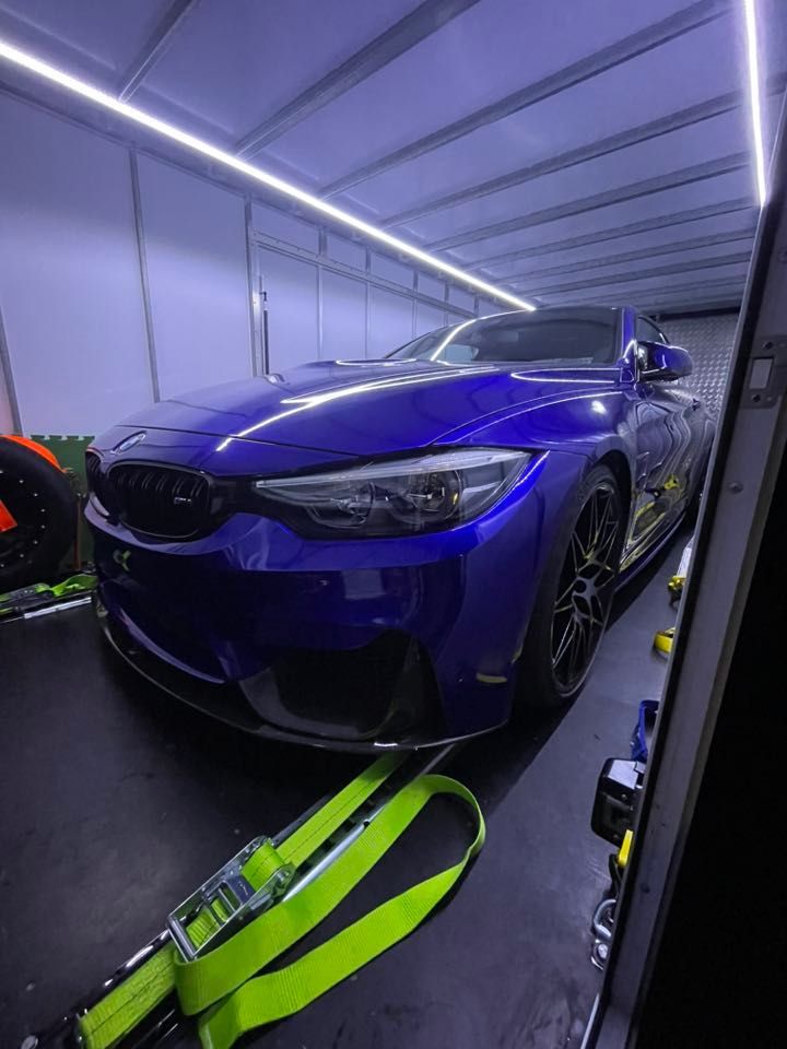 Blue BMW M4 sports car secured inside a trailer with tie-down straps, illuminated by overhead lights — Full Throttle Enclosed Car Transport in Kilmore, VIC